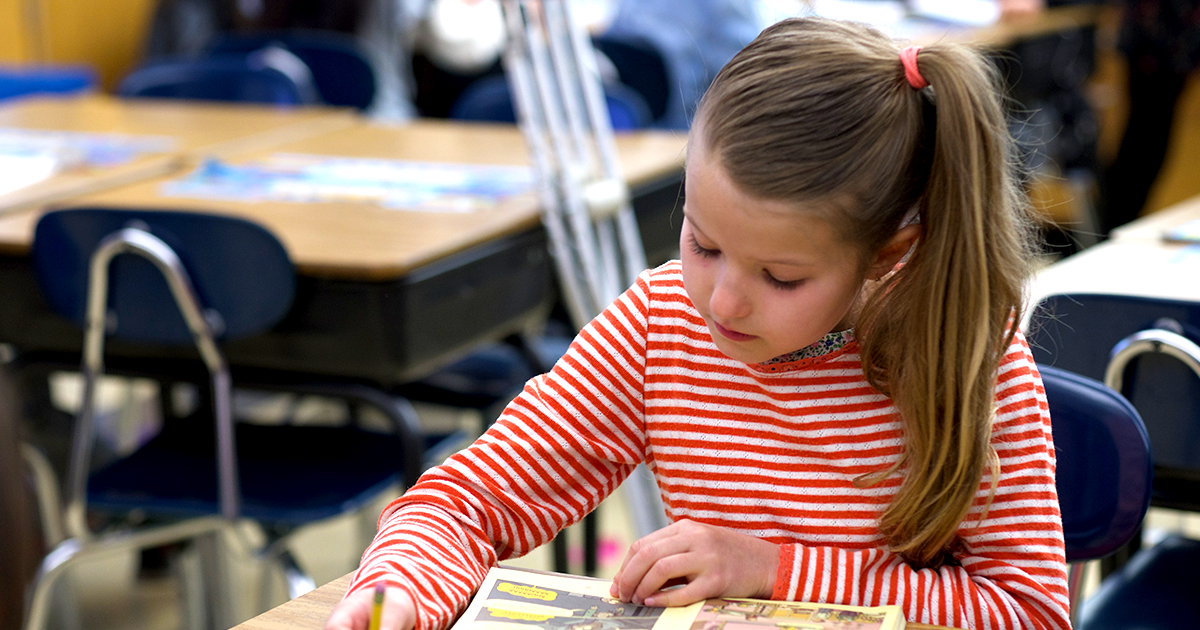 Early elementary students with hands raised